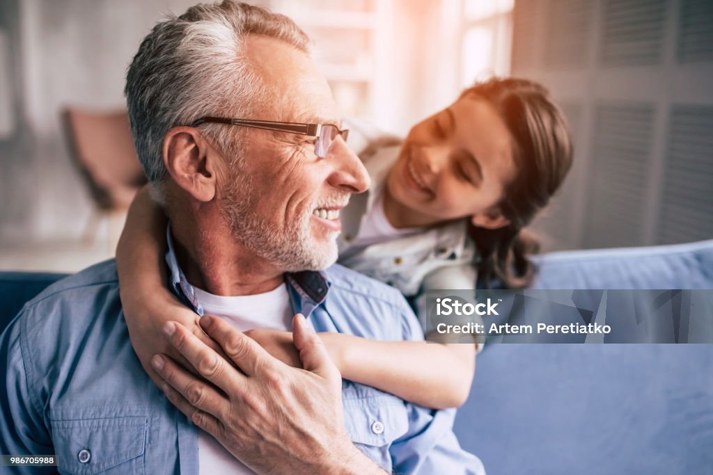 The happy girl hugs a grandfather on the sofa Grandparent Stock Photo