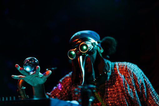 A man is wearing a mask and singing on stage while playing with a crystal ball.