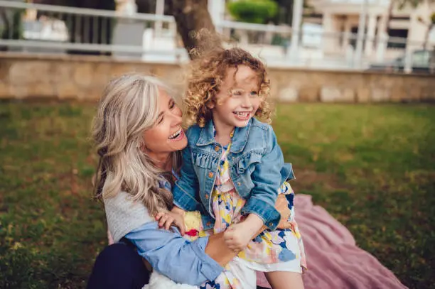 Happy grandmother and little granddaughter embracing, having fun and playing together in park