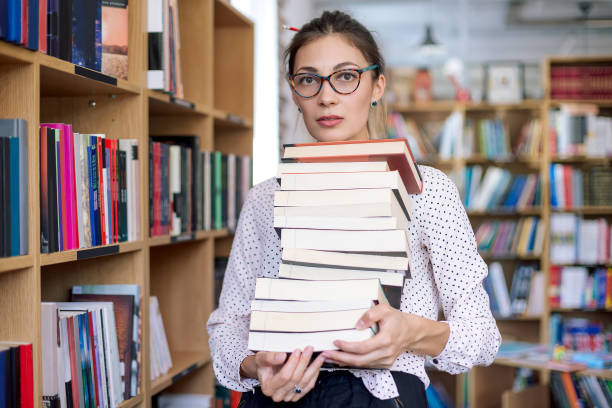 istock Young woman with a stack of books in library 986726584