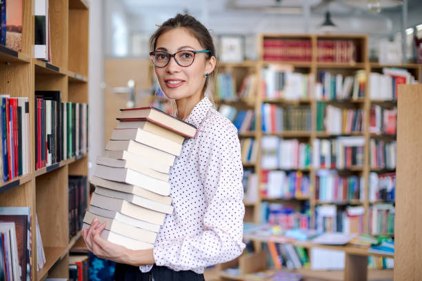 istock Young woman with a stack of books in library 986726666