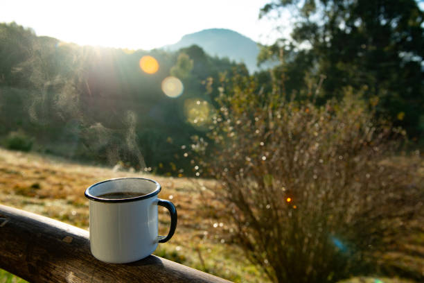 White enameled cup with hot coffee, steaming out on the wooden fence in the farm house