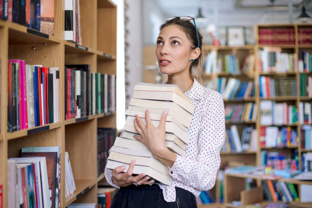 istock Young woman with a stack of books in library 986727882