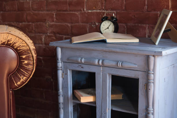 istock Desk clock with a book on a wooden cupboard against a brick wall background 986727940