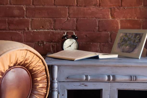 istock Desk clock with a book on a wooden cupboard against a brick wall background 986727996