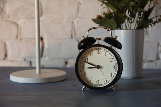 istock Alarm clock with table lamp and flower in pot on nightstand 986728140