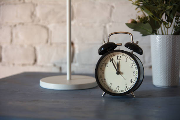 istock Alarm clock with table lamp and flower in pot on nightstand 986728158