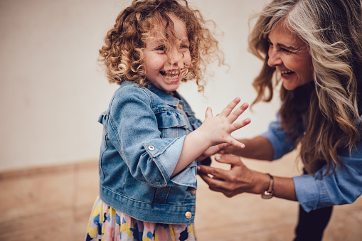 Fashionable retired grandmother and little granddaughter with curly hair having fun, playing and laughing together