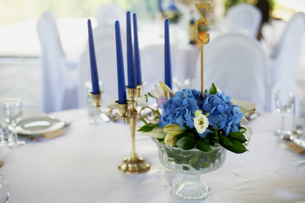 istock Table with a classic design. With a composition in a high vase with hydrangeas and lilies, a Golden candlestick with blue candles.Decor and floristry 986732422