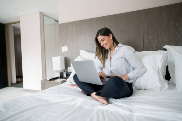 femme d’affaires à domicile travaillant sur un ordinateur portable sur le lit - hotel wireless technology bedroom hotel room photos et images de collection