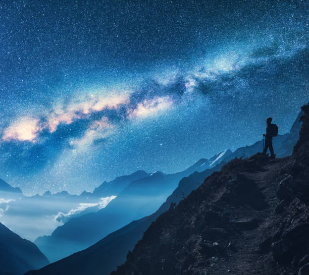 Photo of Milky Way, girl and mountains. Silhouette of standing woman on the mountain peak, mountains and starry sky at night in Nepal. Sky with stars. Trekking. Night landscape with bright milky way. Space
