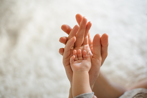 Close up of mother, father and baby join hands on the light background of room
