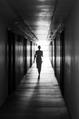 A shot of a woman, intentionally defocused, walking down a poorly lit hallway, with the only source of light behind her.