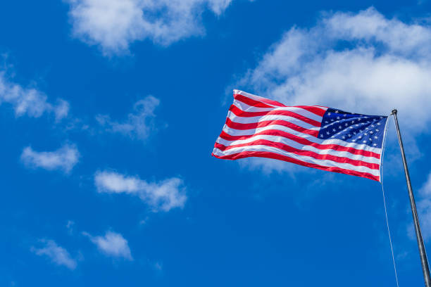 istock American Flag waving with cloudy blue sky on a sunny day 986830330