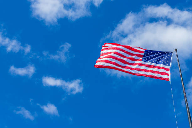 istock American Flag waving with cloudy blue sky on a sunny day 986830442