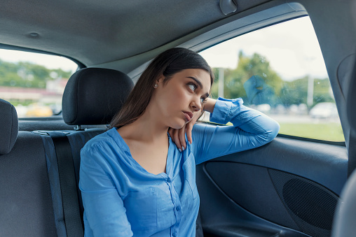 Young woman looking through car window. Woman traveling. Woman at back seat of car looking out window. Sad young woman in the car