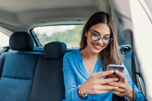 Young girl uses a mobile phone in the car. Technology cell phone isolation. Internet and social media. Woman with smartphone in her car. Girl is using a smartphone