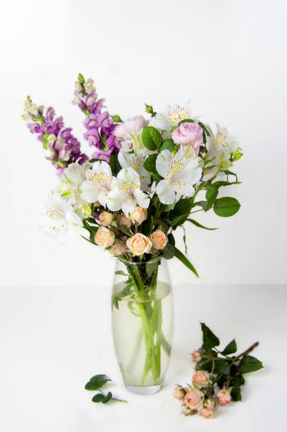 bouquet of fresh flowers of snapdragon, roses, alstroemeria in a glass vase on light background stock photo