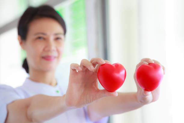 istock Red heart held by smiling female nurse's hand, representing giving effort high quality service mind to patient. Professional, Specialist in white uniform concept 986878882