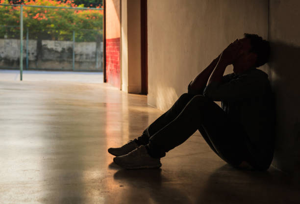 istock Emotional moment: man sitting holding face in hands, stressed sad young male having mental problems, feeling bad, depressed, disappointed, hopeless. Desperate man in the dark corner needing help. 986878962