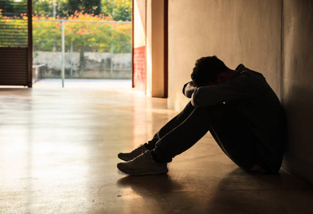 Emotional moment: man sitting holding head low on knees, stressed sad young male having mental problems, feeling bad, depressed, disappointed, hopeless. Desperate man in the dark corner needing help.