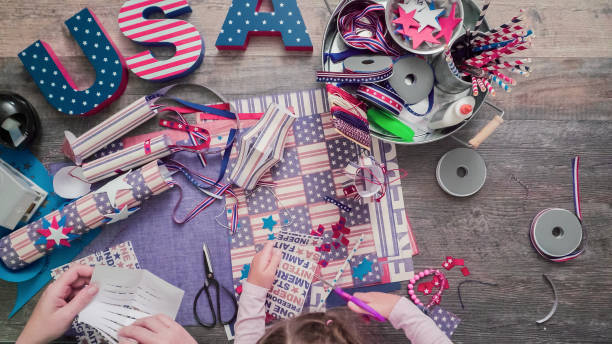 istock Mother and daughter making paper firecrackers fro July 4th celebration. 986930840