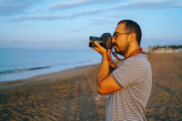 istock Young man taking photos on the beach at sunrise 986938994
