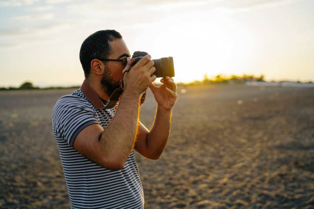 Young man taking photos on the beach at sunrise