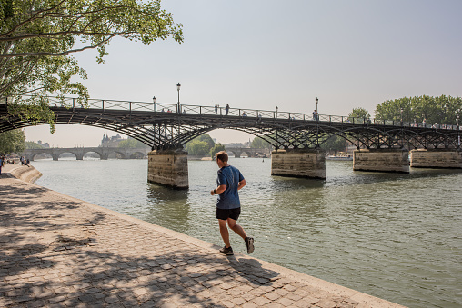 Paris / France - May 19, 2018: A man goes for a jog along the quay at the Seine River, on a beautiful morning.
