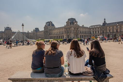 Paris / France - May 19, 2018: A group of young women friends take a break while sightseeing at the Louvre, to talk and check their phones.