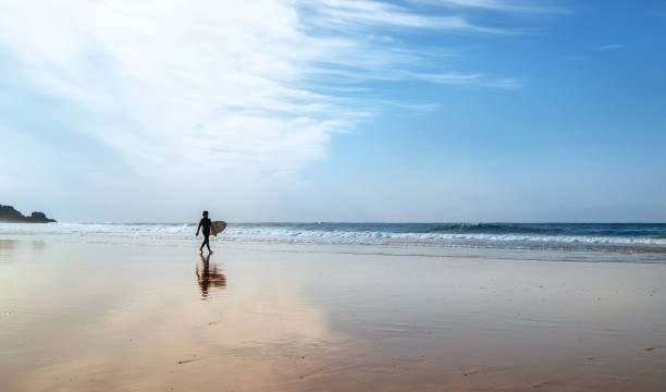 istock Surfer with surfboard walks on coast line 986964220