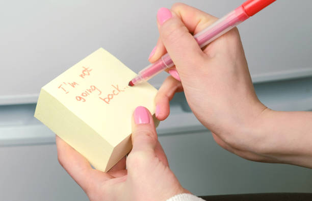 istock Closeup woman's hands write on yellow sticker paper sheets words i'm not going back. 987003346