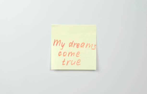 istock Note on yellow sticker paper sheets with motivation words my dreams come true. 987007580