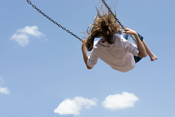 Child swinging high against blue sky stock photo