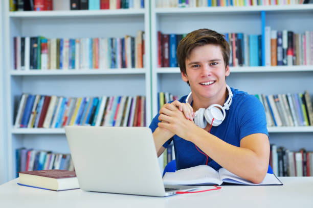 istock Portrait of happy student while reading book in school library. Study lessons for exam. Hard worker and persistance concept. 987045178
