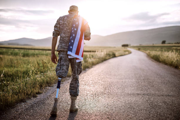 American Amputee Soldier On Road Rear View Of Young Amputee Soldier Walking Road Wearing American Flag war veteran stock pictures, royalty-free photos & images