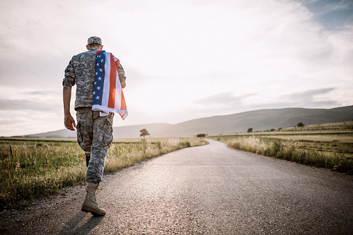 Rearview of a patriotic young soldier walking towards his house with his luggage. Courageous American serviceman coming back home after serving in the military.