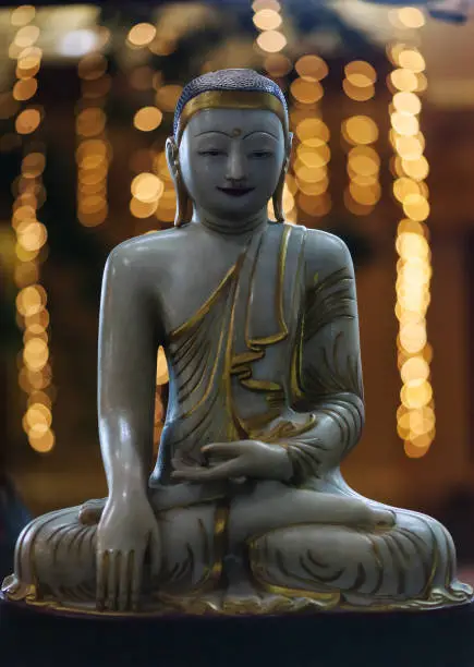 Buddha's figure made of marble in the Burmese style against the background of
 city lights.