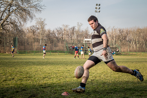Picture of white young caucasian tall male rugby player shooting at a ball doing a drop goal while training for the Belgrade Partizan team. Also known as field goal or pot, a drop goal is a method of scoring points in rugby union and rugby league