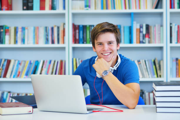 istock Portrait of happy student while reading book in school library. Study lessons for exam. Hard worker and persistance concept. 987107180
