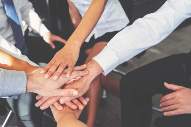 Group of business people joining hands. They are sitting in a circle, putting their hands together. All are unrecognizable. Teamwork concept. All are in corporate business clothing