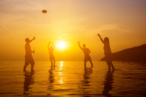 Silhouette image of authentic young people in warm climate drinking, having a party and playing on the beach in summer sunset