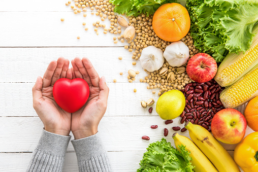 Manos de mujer mostrando bola de corazón rojo con alimentos sanos a un lado photo