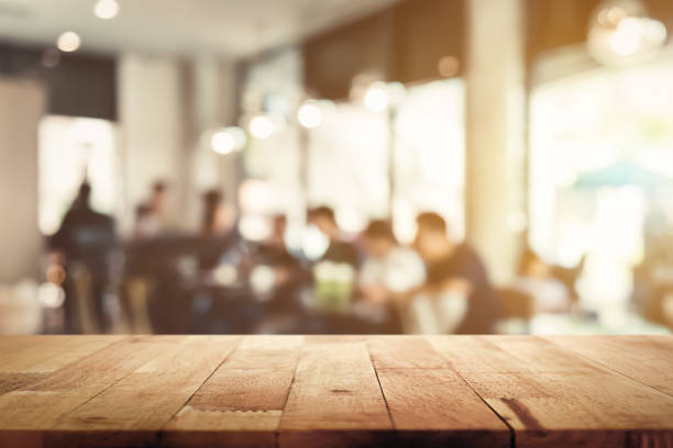 istock Wood table top with blur cafe interior and people in background 987130430