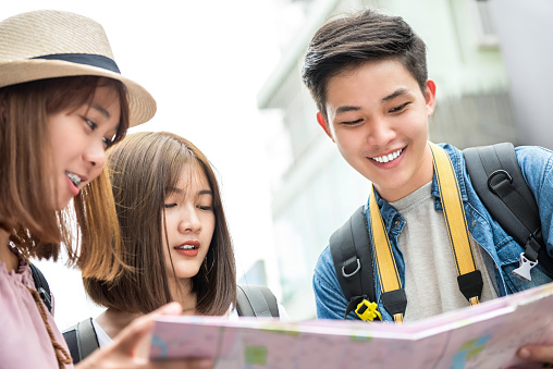 Group of Asian friend tourists looking for direction on the map while traveling together in summer holiday
