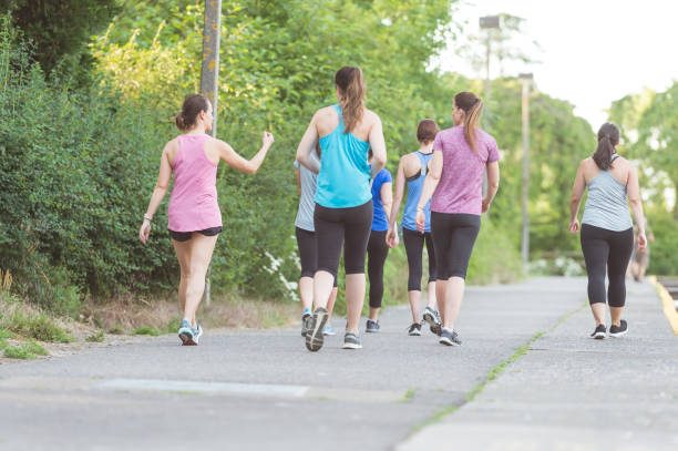 Fundraising Run Group of women participate in a race run/walk to raise money for breast cancer research. They are on a sidewalk, with trees on the left side. The shot is from behind. walking for a cause stock pictures, royalty-free photos & images