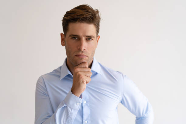 istock Pensive young man touching chin and looking at camera 987268768