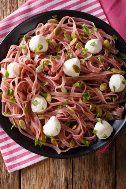 Noodles with beetroot juice with mozzarella, pumpkin seeds and greens close-up. Vertical top view