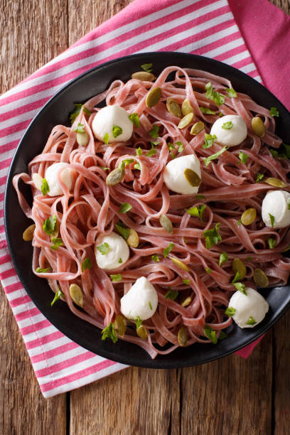 Beetroot pasta with mozzarella cheese, pumpkin seeds and parsley closeup. Vertical top view