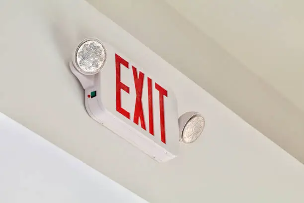 A red exit sign with emergency lights shows above a door.